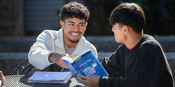 Male student smiling at another student reading a book