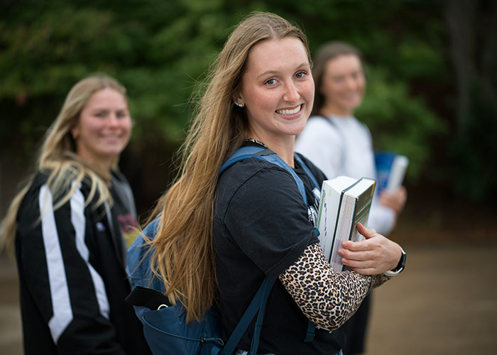 Female Coe student smiling to camera in front of out of focus students