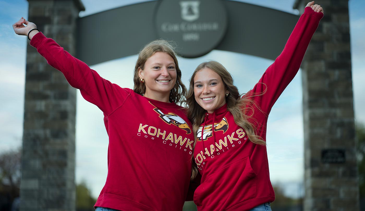 Two female Coe students cheering in front of Coe College arc