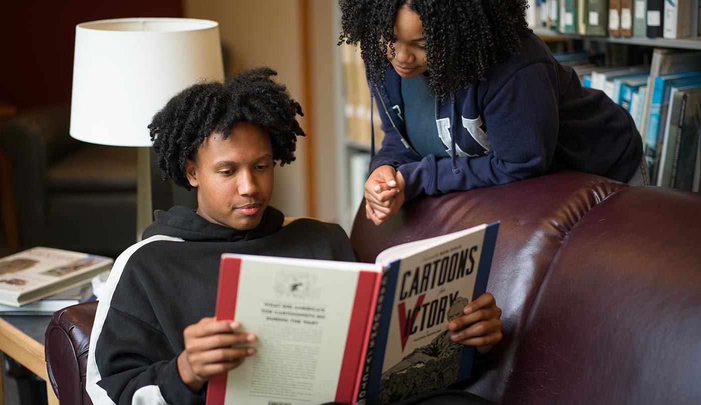 Female student leaning over male student reading