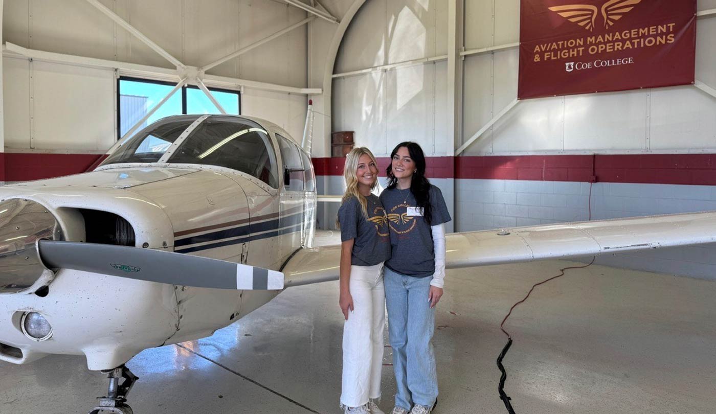 Two female aviation students standing in front of a plane in Coe hangar