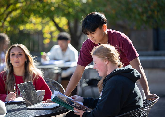 Male student leaning over female student reading