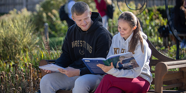 Female and male student sitting on a bench and looking at a book together